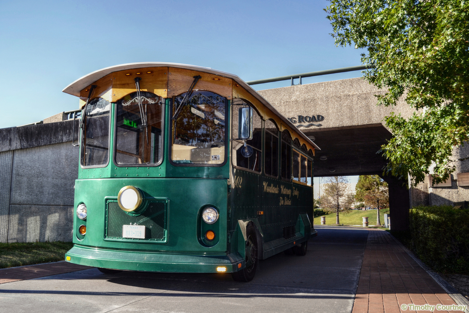 A green Woodlands waterway trolley drives under a bridge near the Riverwalk