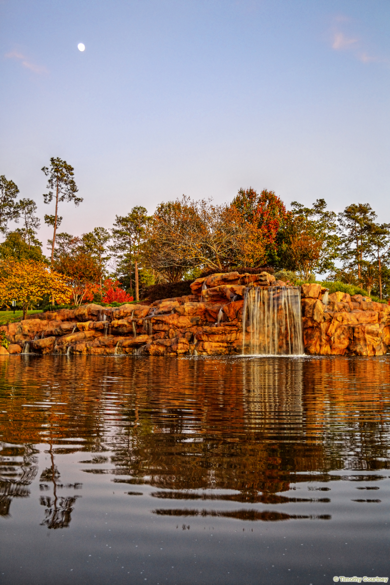 This is a landscape photo of a park pond with a waterfall reflecting into the water