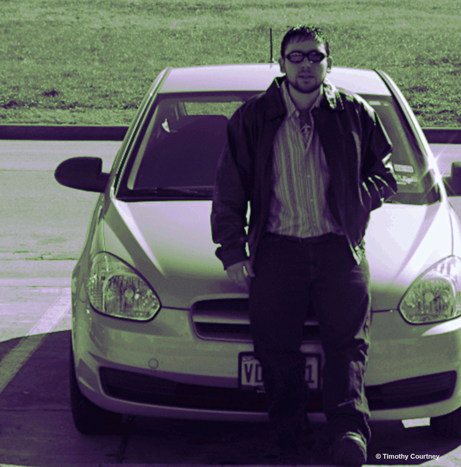 Artist Timothy Courtney wears sunglasses and a leather jacket outside standing next to a car