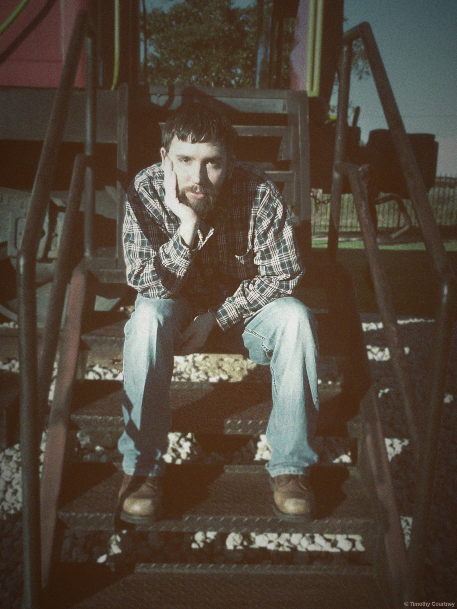 Timothy Courtney wears jeans, boots, and a flannel at the steps of a train car
