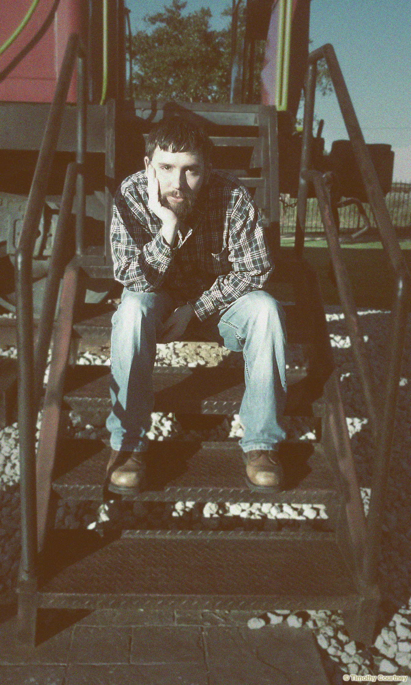 Timothy Courtney is sitting by a train wearing boots and a flannel