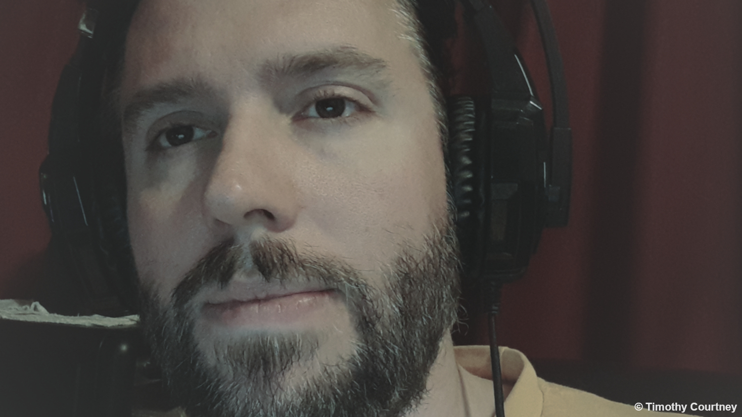 This is a close up facial photo of Timothy Courtney wearing a headset in a yellow tshirt.