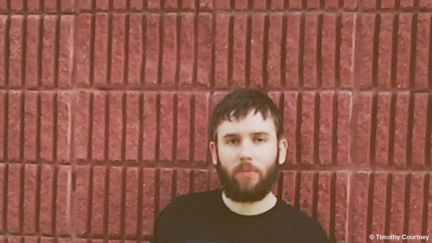 Photo of Timothy Courtney standing in front of a red brick wall