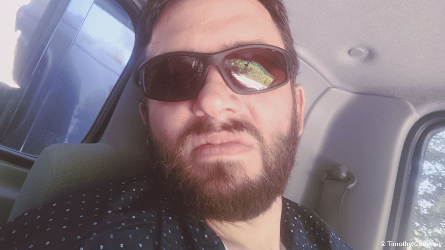 This photo shows Timothy Courtney driving a truck with sunglasses and a blue button up shirt