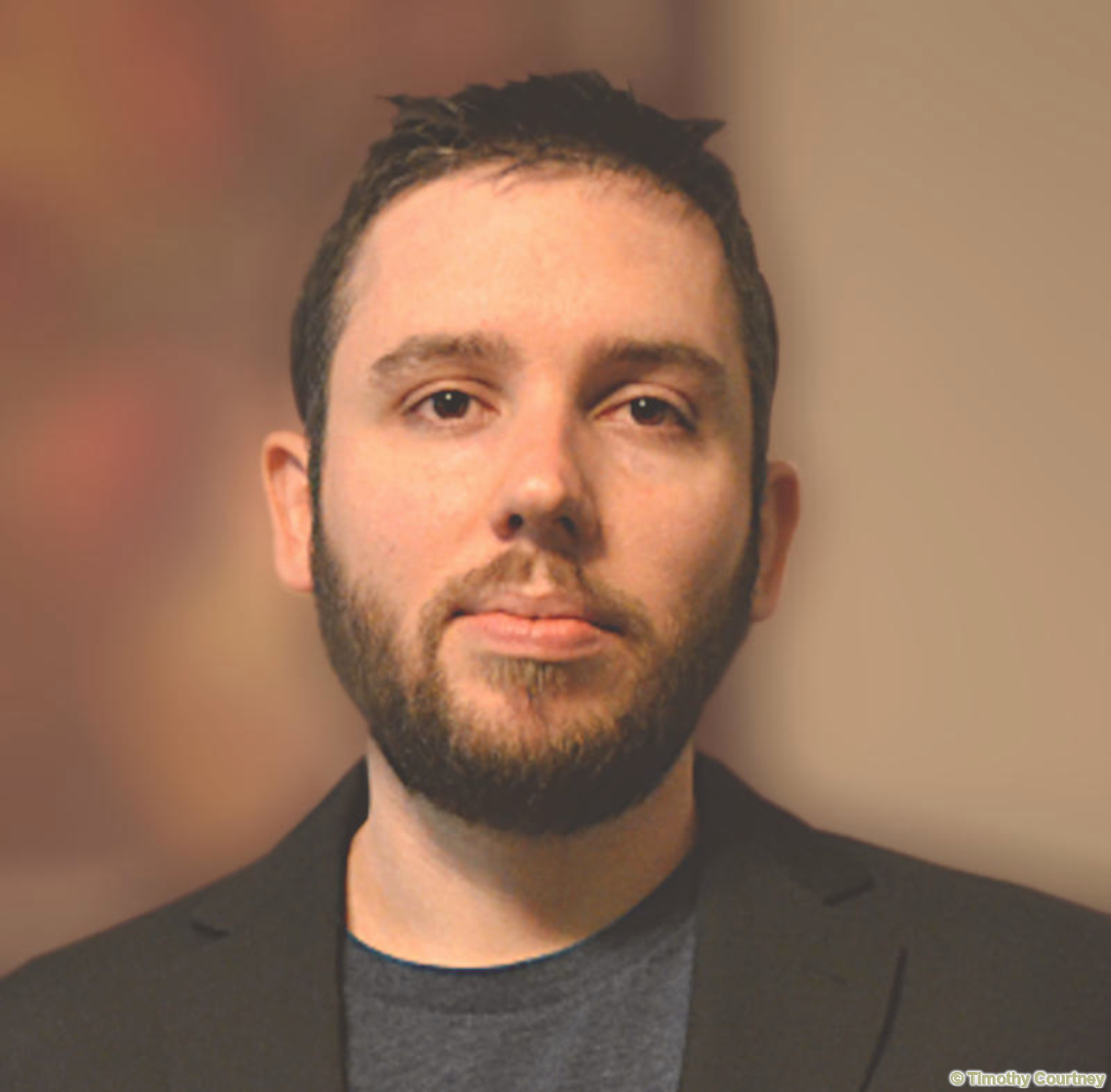 In this portrait of Timothy W Courtney, he is wearing a blue shirt and black overcoat, as he looks into the camera.